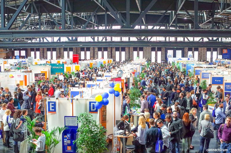 Messehalle mit Ständen und vielen Besuchern unter dem Stahldach