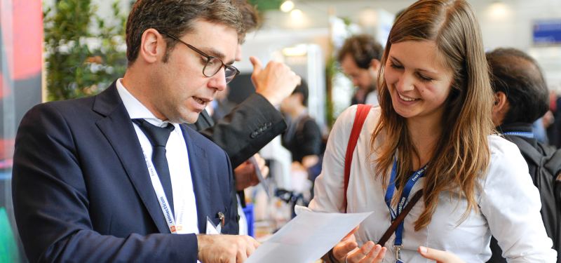 Lachende Besucherin geht mit ihrem Gesprächspartner ein Blatt Papier durch