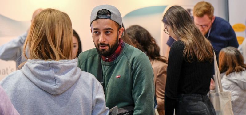 Ein junger Mann mit Basecap spricht mitten im Messegedränge mit einer Besucherin